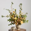 Tall yellow floral arrangement in a ribbed ceramic vase with a matching bowl on a table