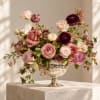 Pink and burgundy roses arranged in a silver pedestal vase
