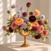 Mixed bouquet in a gold pedestal vase with peach, pink, purple, and burgundy blooms