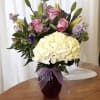 Pink roses and white hydrangeas in a purple vase with a ribbon