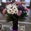 A purple vase with roses, daisies, carnations, and purple filler flowers for