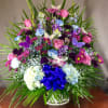 Colorful mixed flower arrangement in a white basket with a blue bow