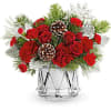 Red roses and carnations in a clear glass vase with pinecones