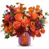 Orange roses and mixed fall flowers in a striped glass vase
