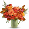 Orange and coral roses with mums in a green ceramic pitcher