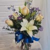 Bouquet of white lilies, cream roses, and purple flowers in a glass vase