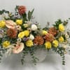 Mixed floral arrangement in a white rectangular vase with yellow and peach blooms