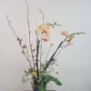 Tall orchid arrangement in a ribbed metal vase with branches and round yellow accents