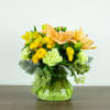 Yellow and peach floral arrangement in a green glass vase