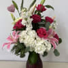 Pink roses and lilies arranged in a dark glass vase with white hydrangeas.