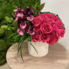 Hot pink roses and purple calla lilies in a white cylinder vase on a wooden table