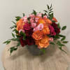 Low arrangement of orange, pink, and red roses in a gray bowl on a wooden table