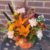 Autumn flower arrangement in an orange pumpkin container with lilies and mums