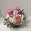 Low arrangement of pink peonies and roses with white hydrangeas in a clear glass vase