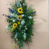 Standing floral spray with sunflowers, blue and white flowers, and greenery
