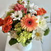 Mixed bouquet of orange roses, daisies, and pink blooms in a white vase