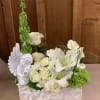 White floral arrangement with roses, lilies, and a cherub figurine in a white container