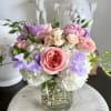 Pastel bouquet of roses, hydrangeas, and purple blooms in a glass vase