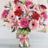 Bouquet of pink and red flowers in a clear glass vase with a pink ribbon