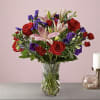 Bouquet of red roses, pink lilies, and purple flowers in a glass vase