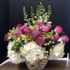 Pink roses and green orchids arranged with white hydrangeas in a patterned vase