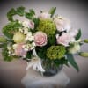 Pink and white roses arranged in a glass vase with green blooms