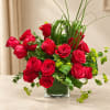 Red roses arranged in a clear square vase with tall grass accents