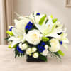 White lilies and roses with blue accents in a black square vase