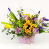Mixed bouquet in a pink basket with yellow, purple, and lavender flowers