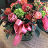 Pink and coral bouquet with roses, gerbera daisies, and a ribbon in a glass vase