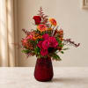 Mixed bouquet of roses and orange daisy-like flowers in a red vase
