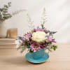 Small floral arrangement in a blue teacup and saucer with a white rose and pink daisies