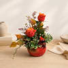 Two red roses in a red ceramic vase with autumn foliage