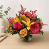 Bright mixed bouquet in a clear glass vase with pink, yellow, and orange flowers