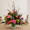 Mixed bouquet of roses, carnations, and snapdragons in a pale vase
