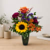 Mixed bouquet with a sunflower, roses, and orange alstroemeria in a dark vase