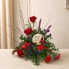 Red roses and purple flowers arranged around a memorial stone on a table