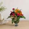Mixed bouquet of orange, pink, and burgundy flowers in a glass vase