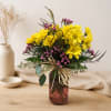 Yellow daisies and pink filler flowers in a glass vase with a raffia bow
