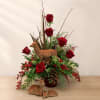 Red roses arranged with pinecones and deer figurines in a vase
