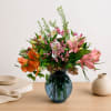 Mixed bouquet of pink, orange, and white flowers in a blue glass vase