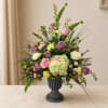 Mixed pink, purple, and white flowers in a dark pedestal vase