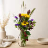 Mixed bouquet with yellow sunflowers and purple flowers in a clear glass vase