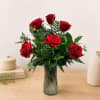 Red roses arranged in a clear glass vase with greenery