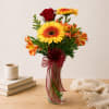 Mixed bouquet of yellow, orange, and red flowers in a glass vase with ribbon