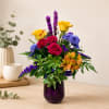 Colorful bouquet of roses, purple spikes, and blue flowers in a purple vase
