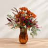 Orange and purple floral arrangement in an amber glass vase