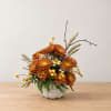 Orange chrysanthemum arrangement in a white pumpkin-shaped vase
