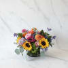 Mixed bouquet with sunflowers, roses, and purple blooms in a low vase