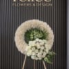 White floral standing wreath on an easel with roses and greenery